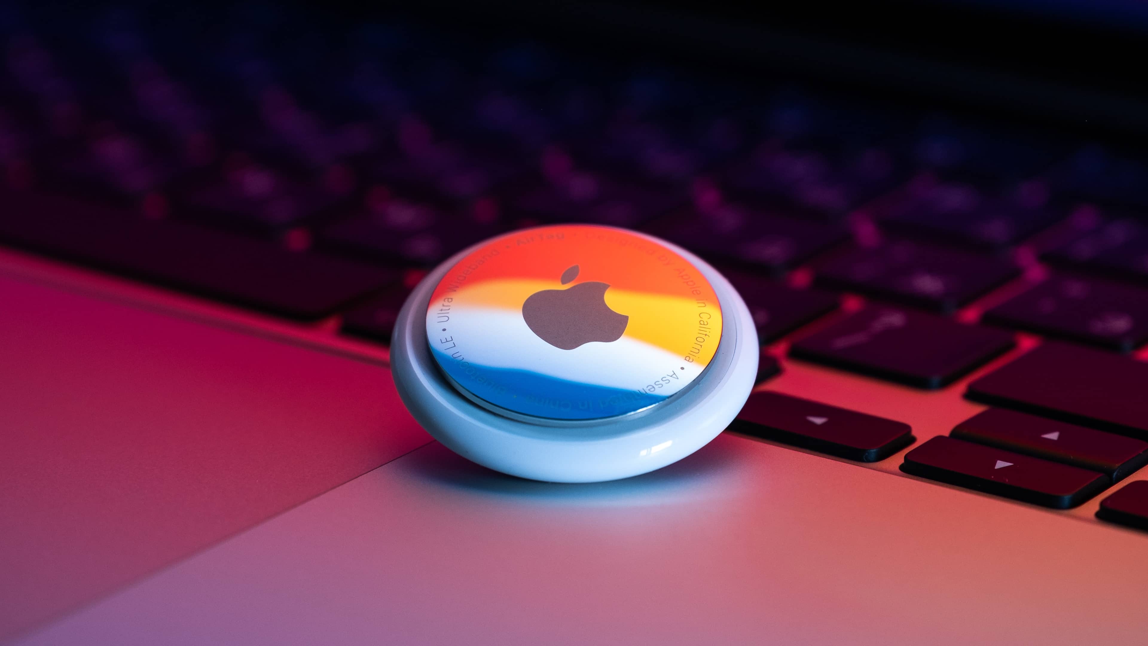 Apple's AirTag personal tracker laid facedown on a Magic Trackpad with the rainbow light pattern reflecting off of its shiny rear surface