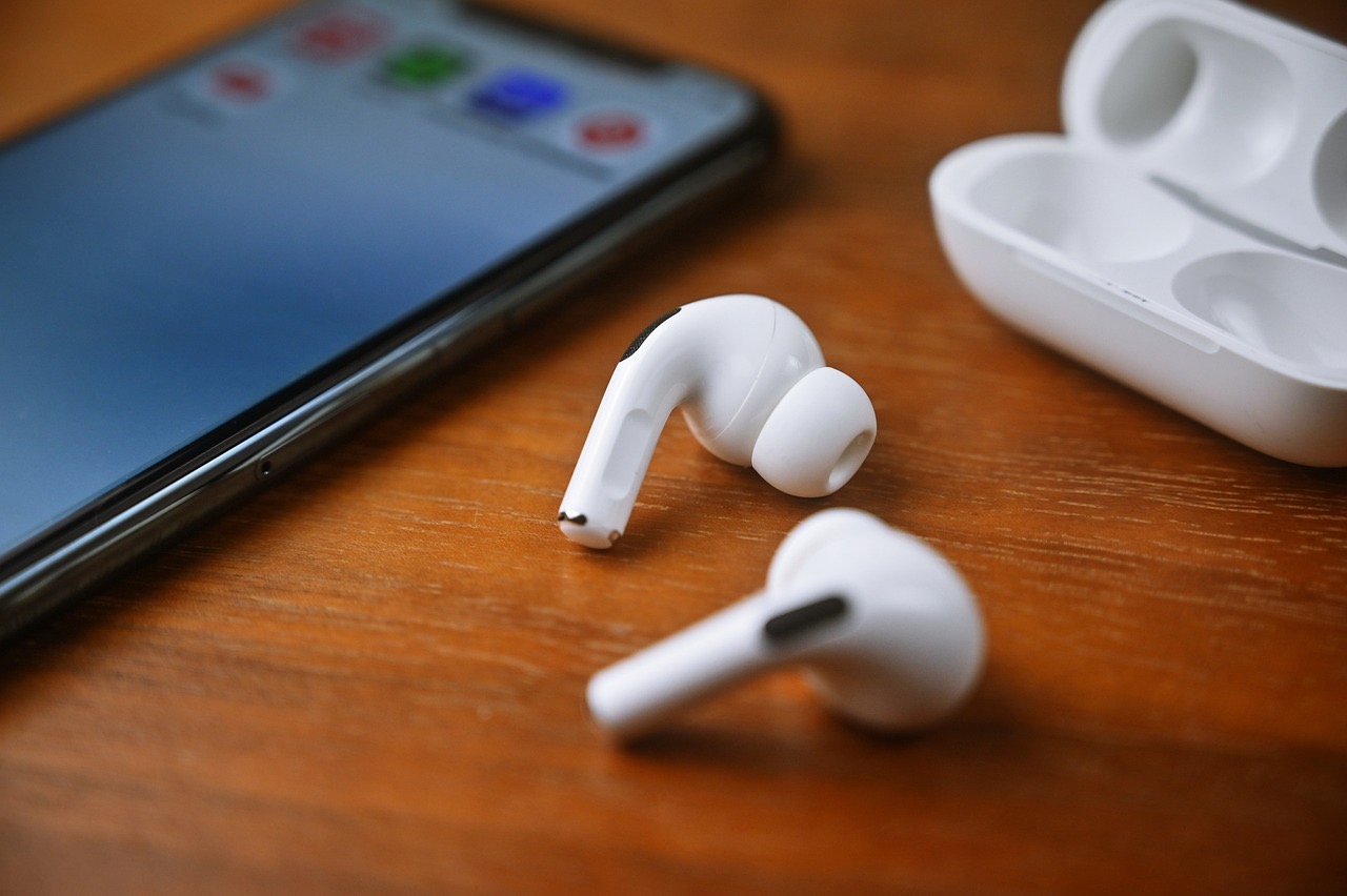 The AirPods Pro earbuds on a wooden desk next to their charging case and an iPhone laid facedown